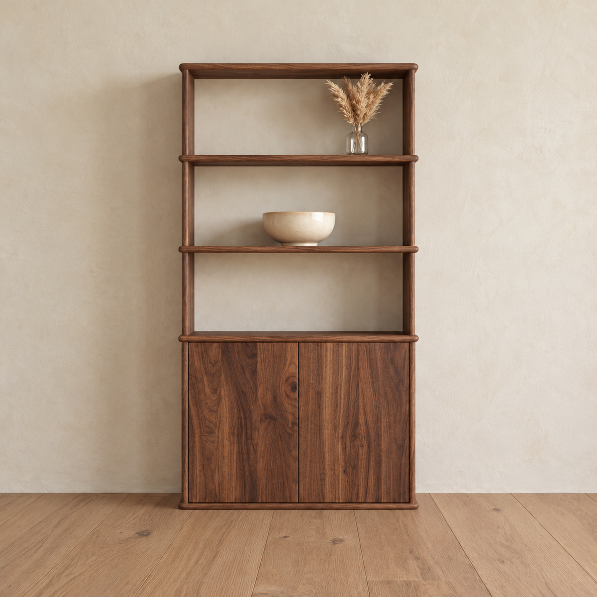 The cabinet bookshelf in walnut against a plaster wall, with three open shelves above a two-door cabinet, holding a small vase of dried grass and a bowl.
