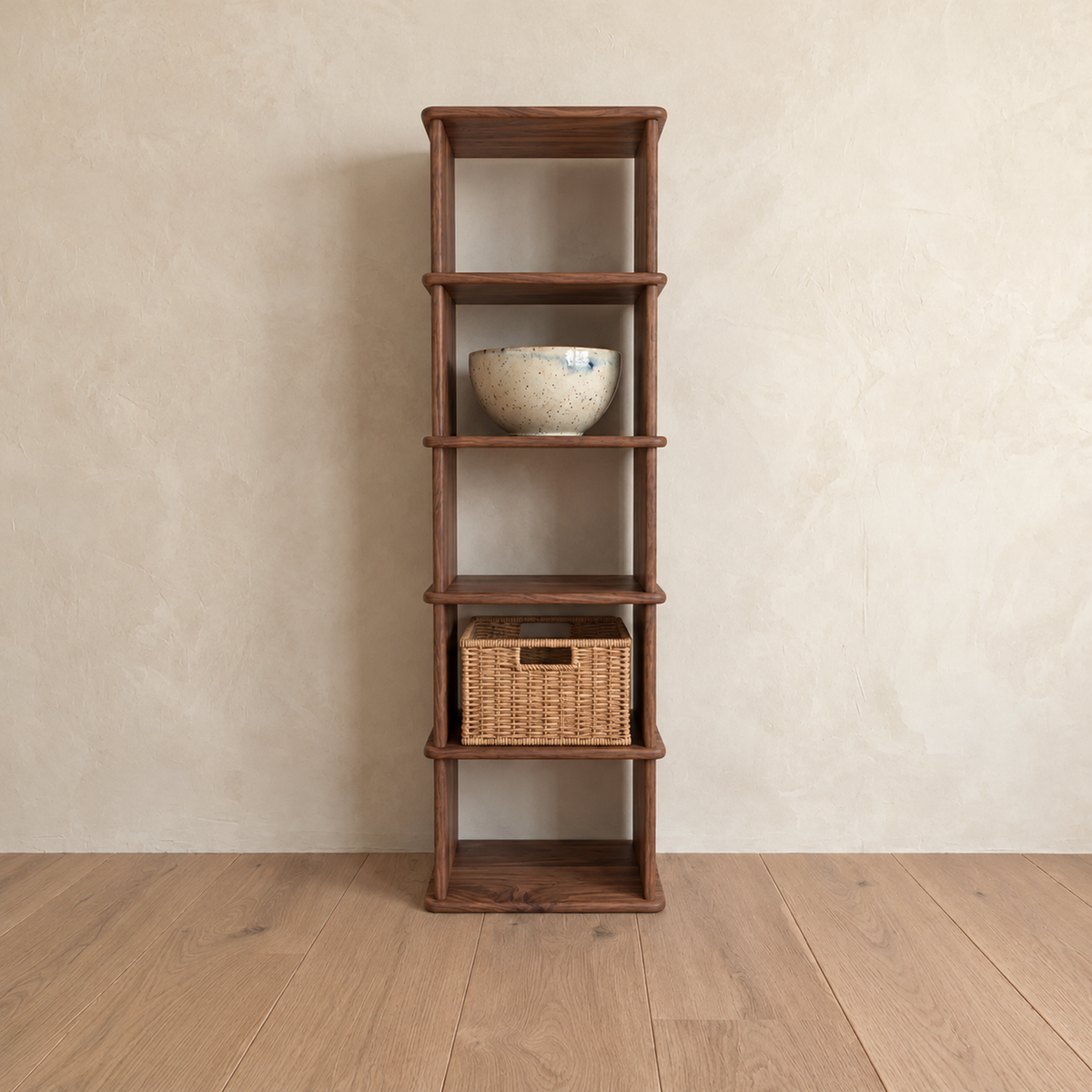 The narrow bookshelf in walnut against a plaster wall, with a ceramic bowl and a woven basket on its shelves.
