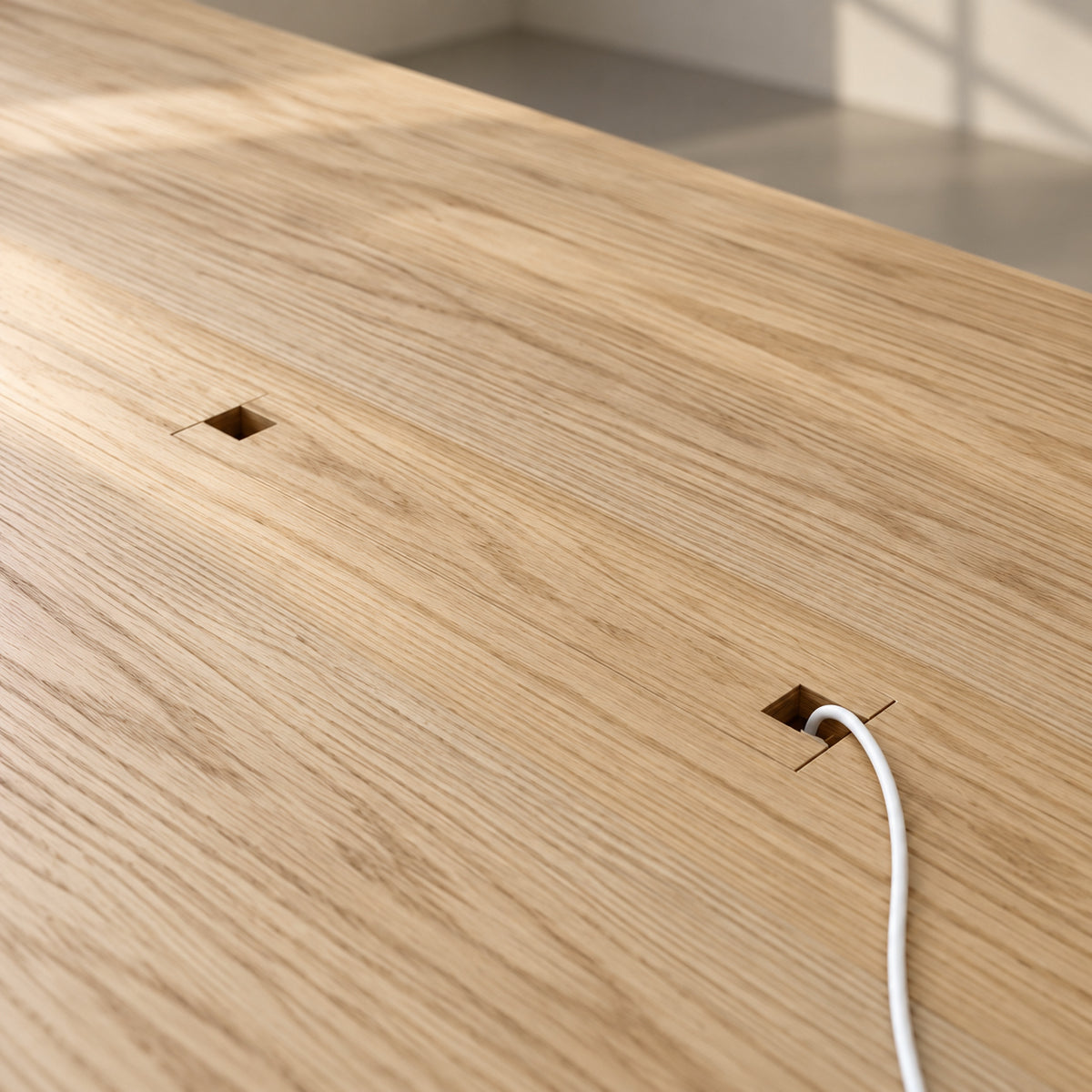 Close-up of the top of the conference table in white oak, showing the small cable openings at each end of the power lid, with a charging cable coming out of one.