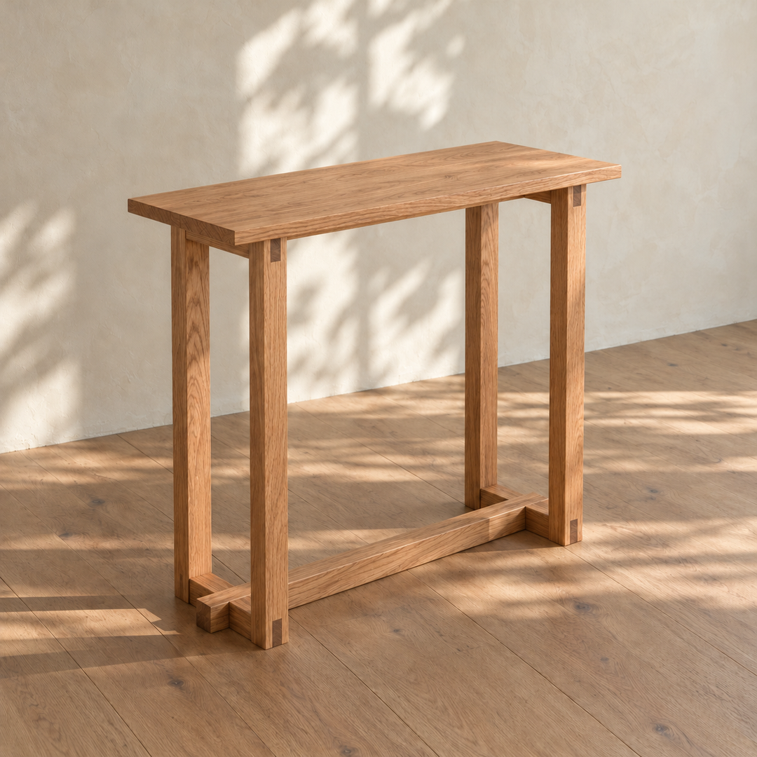 The 2 person bar table in red oak from an angle in dappled sunlight, with its solid top, bridle-jointed leg frames and a long stretcher near the floor.