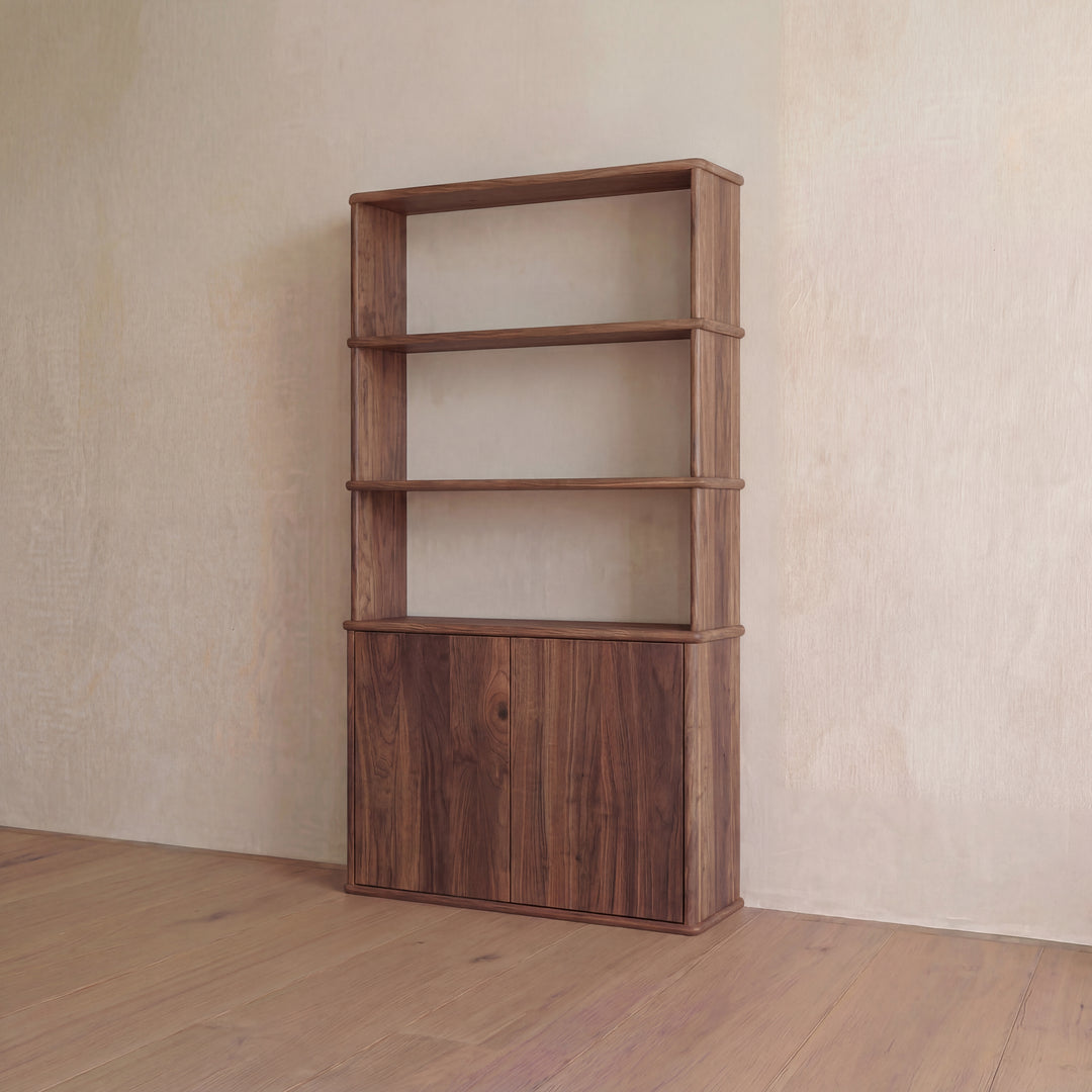 A Cabinet bookshelf in walnut with three open shelves above and a push-to-open closed cabinet below, placed against a plain beige wall on a wooden floor.