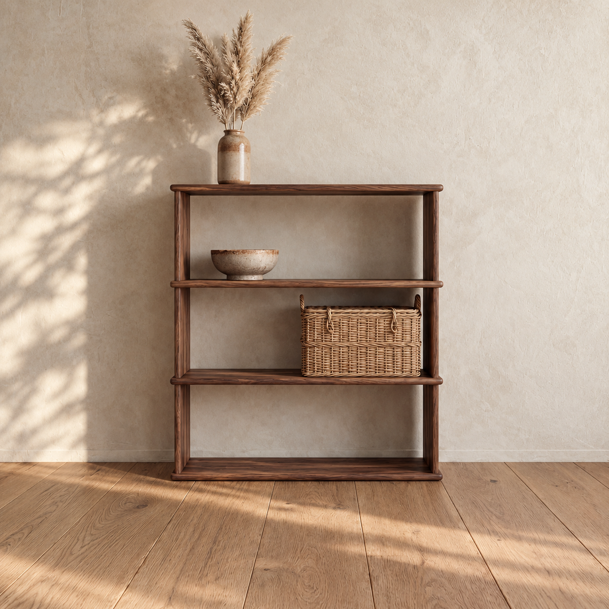The 3 shelf bookcase in walnut against a plaster wall, with a vase of pampas grass on top, a ceramic bowl on the upper shelf and a woven basket on the lower shelf.