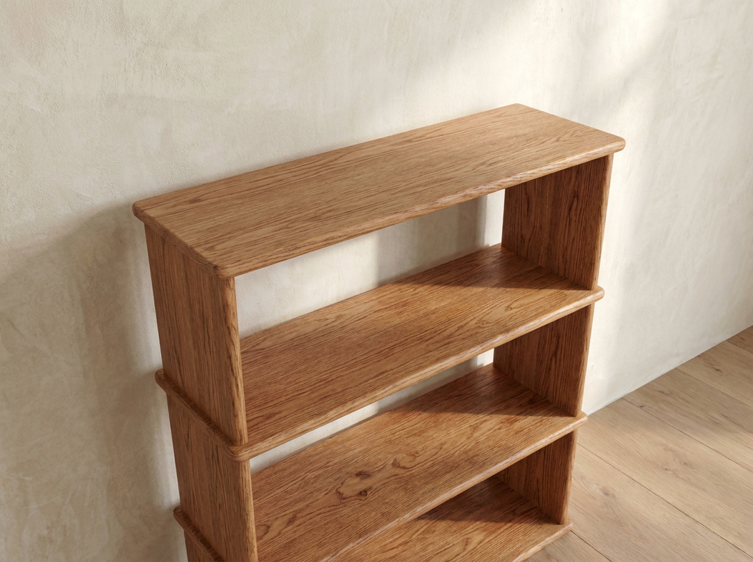 The 3 shelf bookcase in red oak, handcrafted and simple, stands empty against a beige textured wall on a wooden floor, illuminated by natural light.
