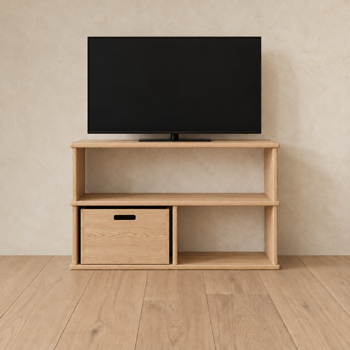 The 40 inch bookshelf TV stand in white oak holding a flat-screen TV, with a wooden storage cube in the lower left opening, against a plaster wall.