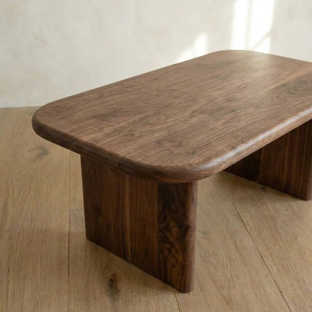 The 40 inch coffee table in walnut features rounded edges and a smooth finish, creating a minimalist look as it sits on a light wooden floor in a softly lit room.