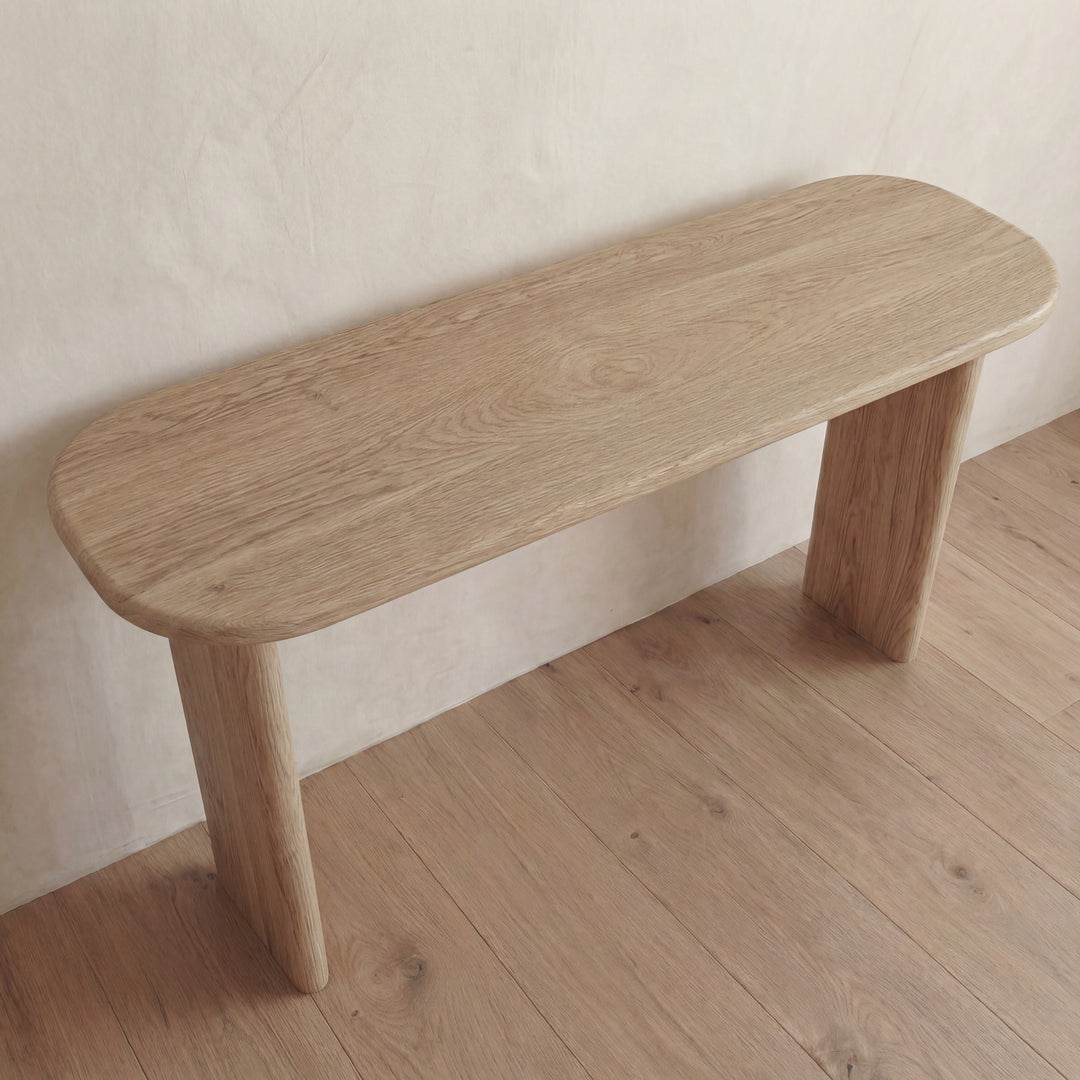 A minimalist 60 inch console table in white oak with rounded edges and sturdy legs, set against a light wall on a matching wooden floor.