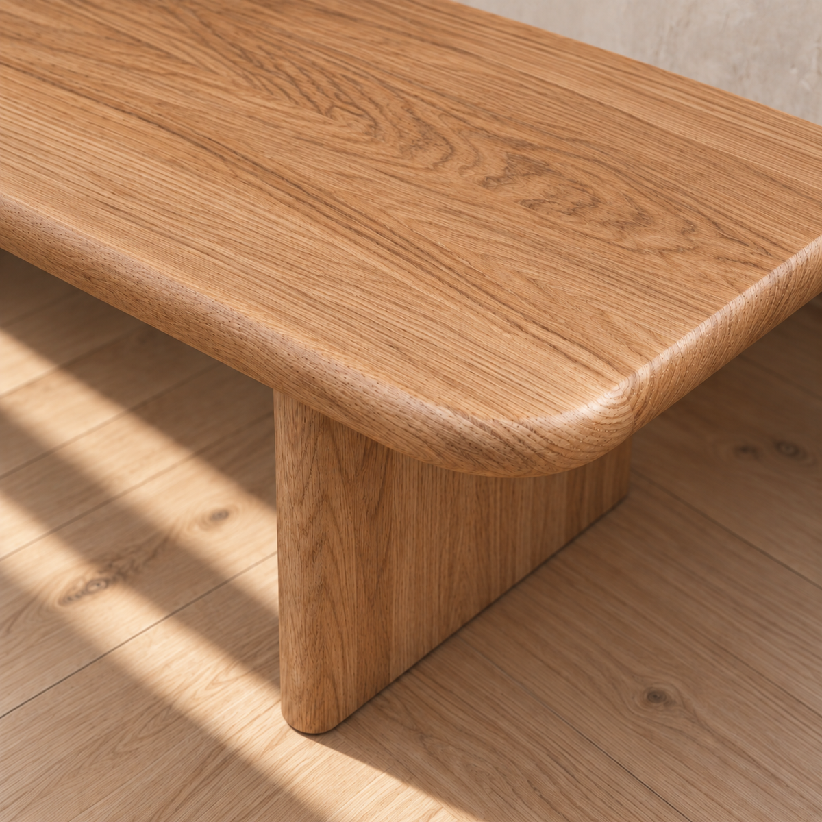 A close-up of the 60 inch coffee table in red oak, showcasing its handmade construction with rounded edges, a smooth surface, and natural wood grain, placed on a matching wood floor in a sunlit room.