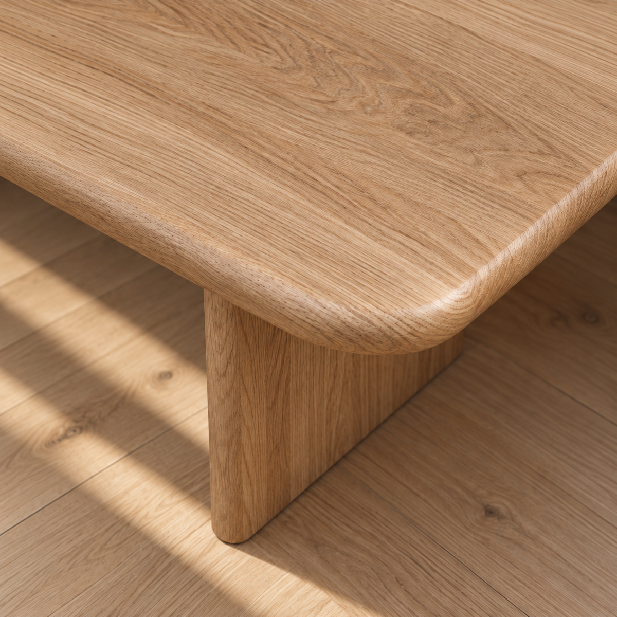 A close-up of the 60 inch coffee table in white oak, featuring a minimalist design with rounded edges and sturdy legs, placed on a matching wooden floor. Sunlight casts soft shadows across the surface and floor.