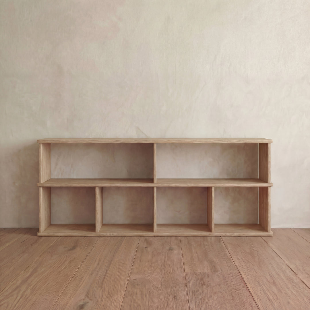 The 65 inch bookshelf TV stand in white oak features six open compartments and stands empty against a light-colored textured wall and wooden floor.