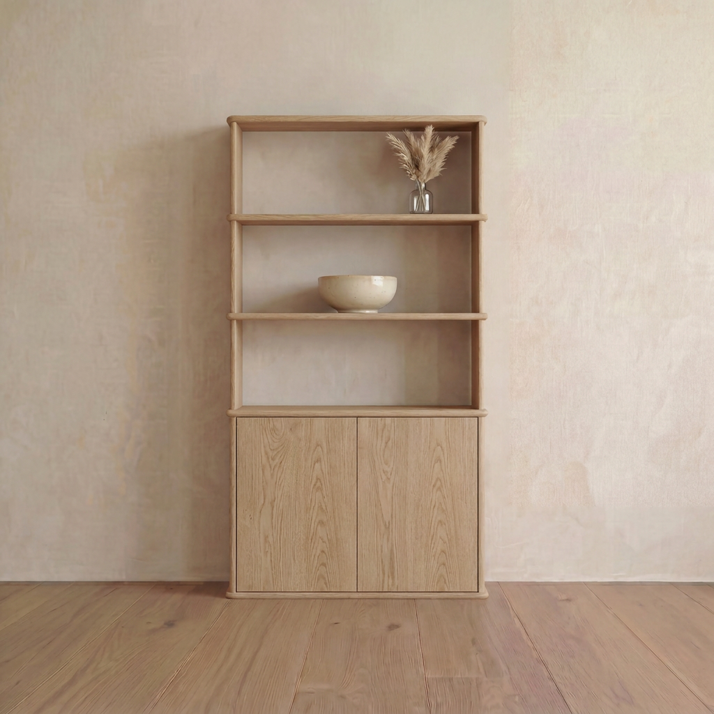 The Cabinet Bookshelf in white oak features a minimalist handmade design set against a neutral wall, with three open shelves—the top displaying a glass vase filled with dried grass, the middle holding a beige bowl—and a closed cabinet at the bottom, encapsulating elegant Vancouver furniture craftsmanship.