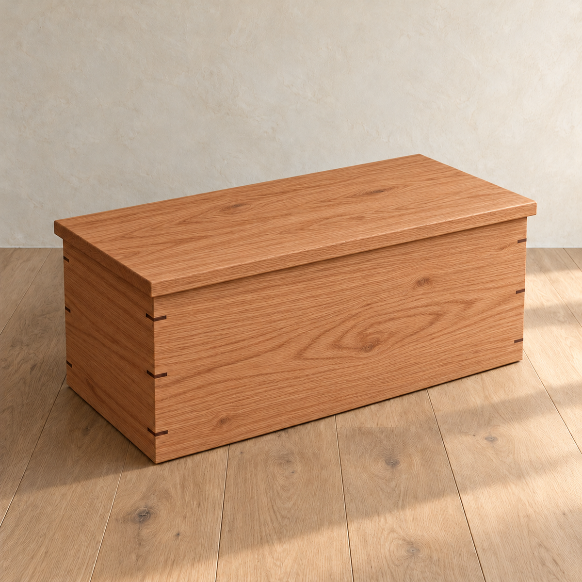 The chest coffee table in red oak with its lid closed, showing the overhanging lid and the walnut keys across its mitred corners.