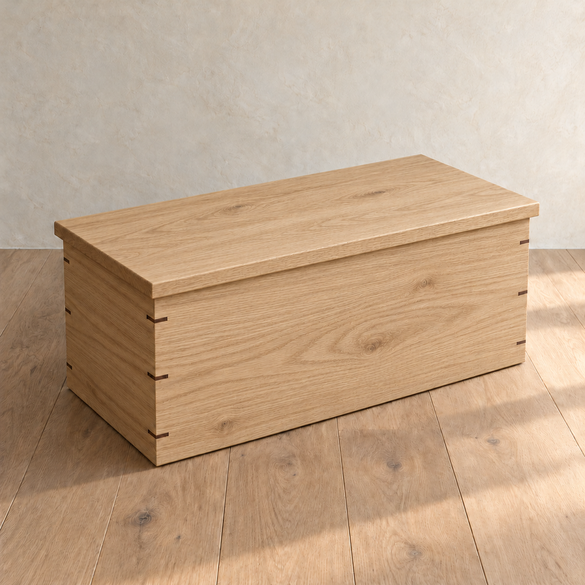 The chest coffee table in white oak with its lid closed, showing the overhanging lid and the walnut keys across its mitred corners.
