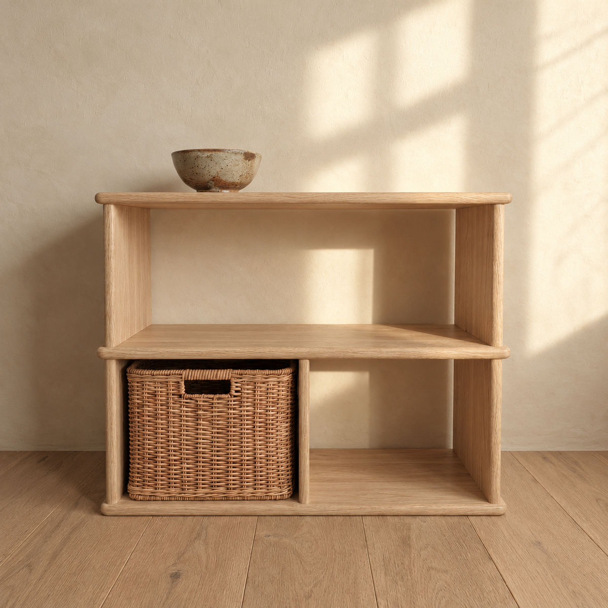 The console bookcase in white oak against a sunlit plaster wall, with a bowl on top and a woven basket in one of the lower openings.
