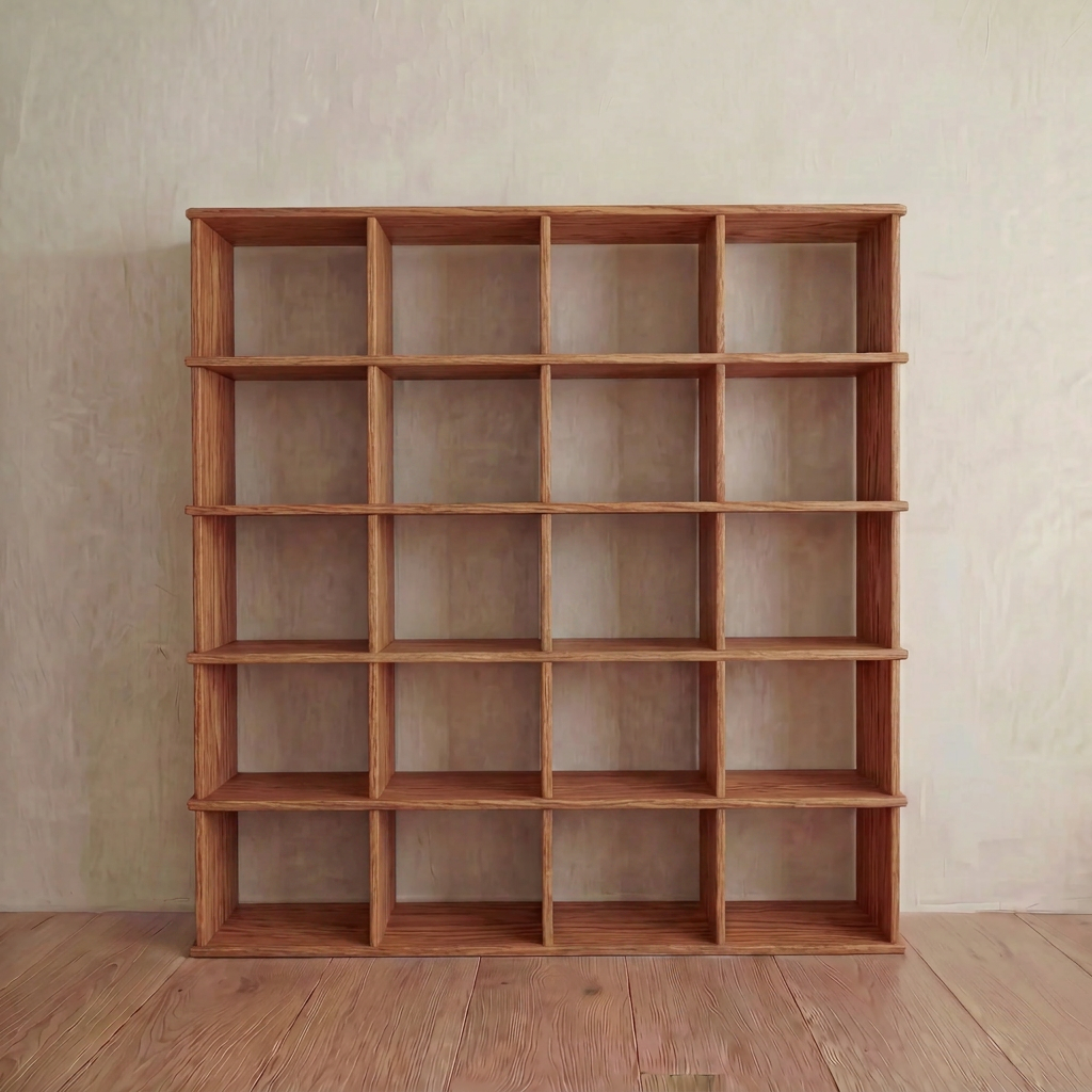 The Cube bookshelf in red oak features five rows and five columns of square, empty compartments and stands against a light-colored wall on a wooden floor.