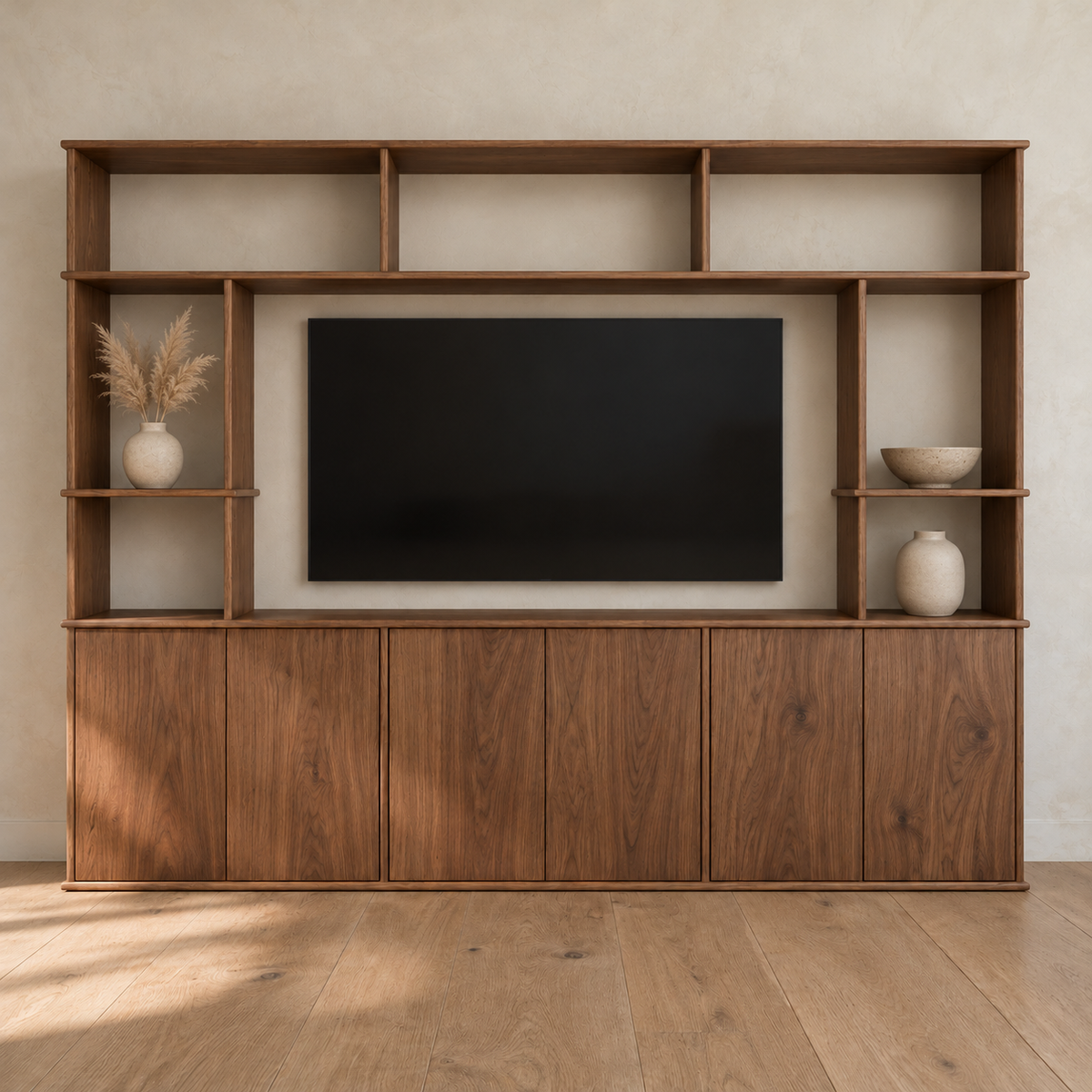 The entertainment center in walnut against a plaster wall, with a TV in the centre opening, pampas grass, small vases and a bowl on its side shelves, and six cabinet doors below.