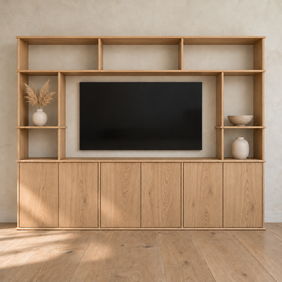 The entertainment center in white oak against a plaster wall, with a TV in the centre opening, pampas grass, small vases and a bowl on its side shelves, and six cabinet doors below.