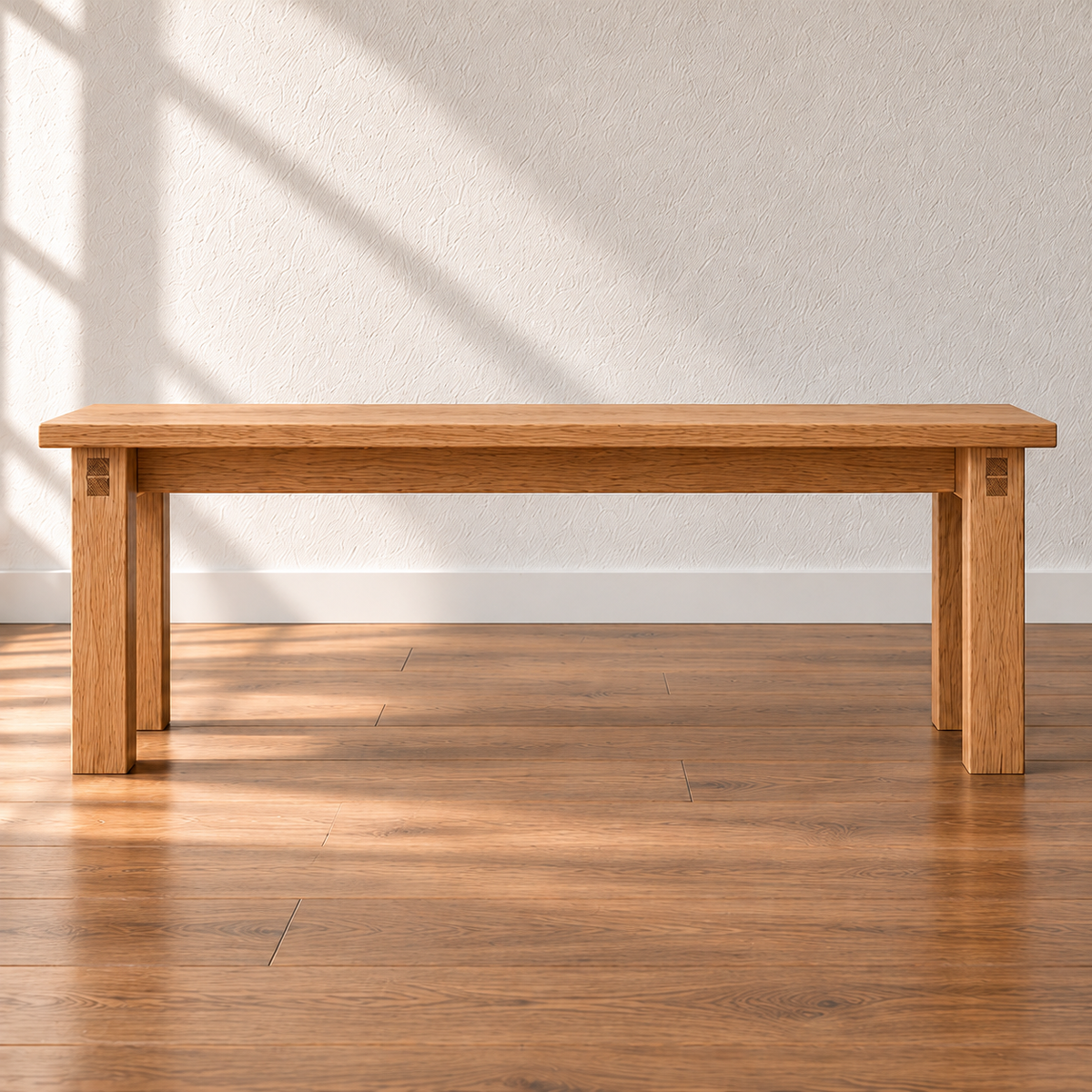 A farmhouse bench in red oak with a thick solid top and four square legs, against a sunlit white wall on a wood floor.