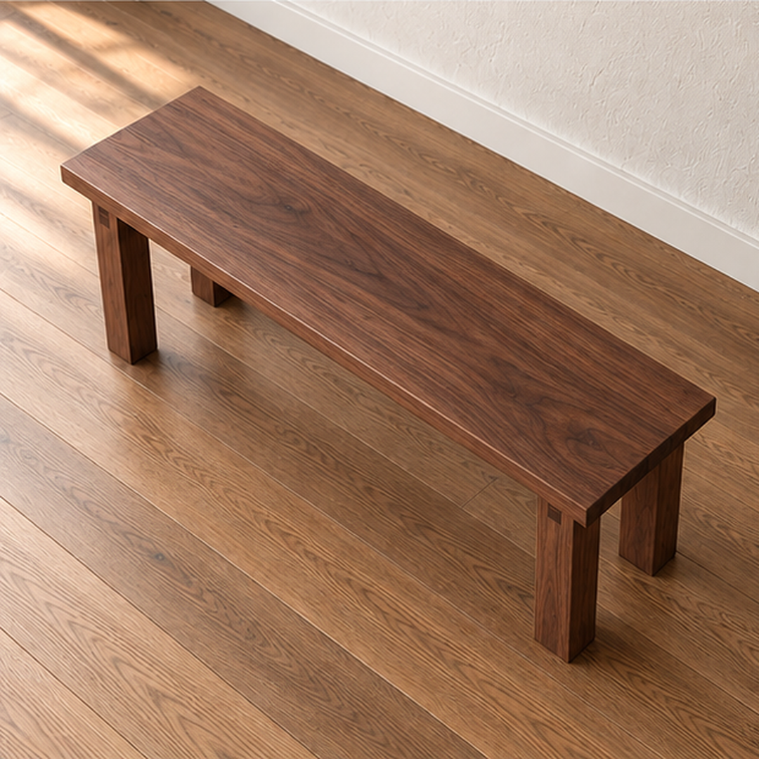 The farmhouse bench in walnut seen from above at an angle, showing the grain running the length of the solid top.