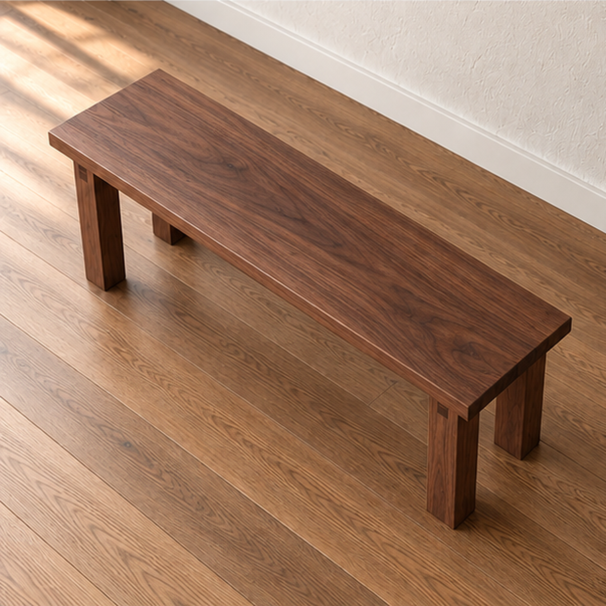The farmhouse bench in walnut seen from above at an angle, showing the grain running the length of the solid top.