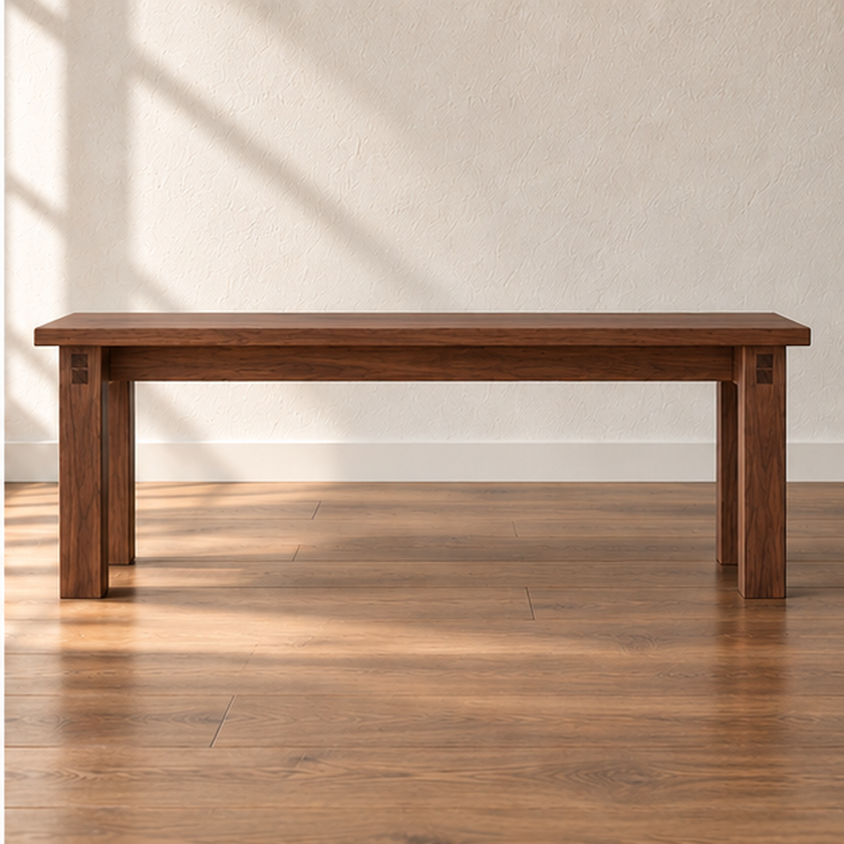 A farmhouse bench in walnut with a thick solid top and four square legs, against a sunlit white wall on a wood floor.