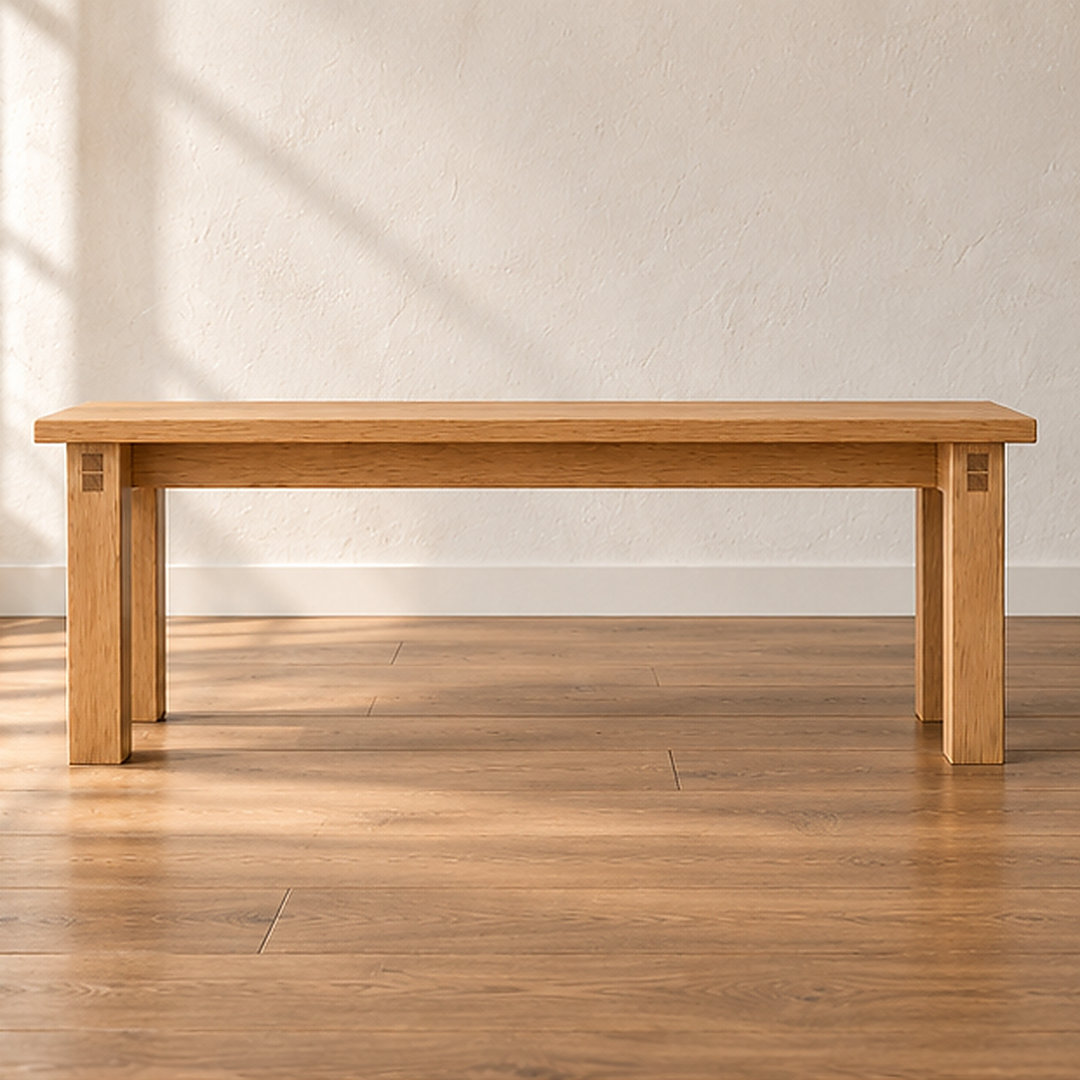 A farmhouse bench in white oak with a thick solid top and four square legs, against a sunlit white wall on a wood floor.