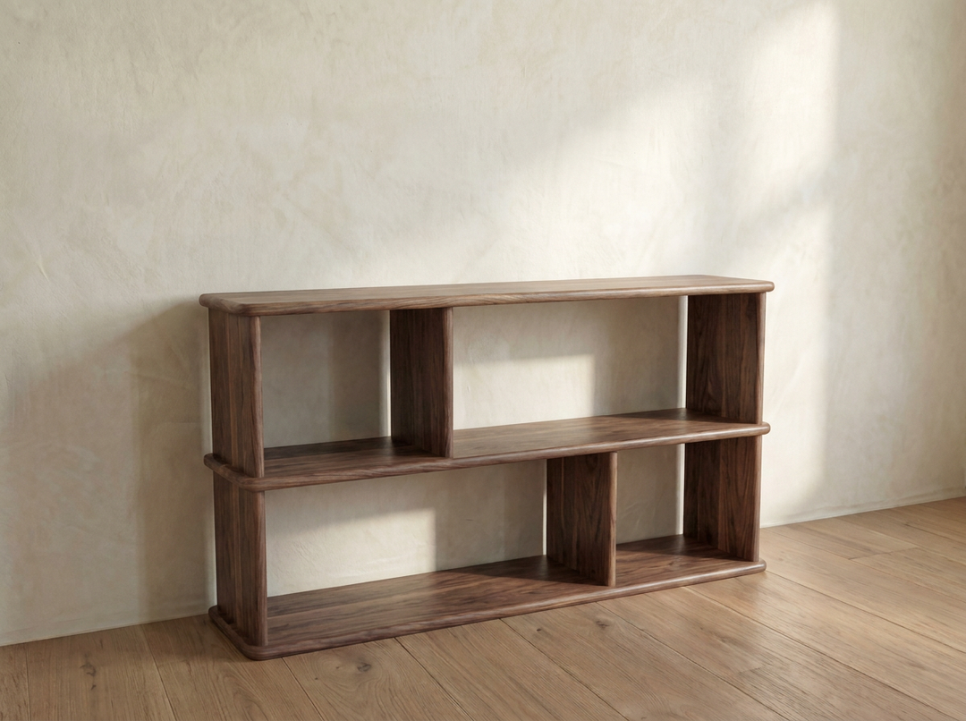 The Horizontal bookshelf in walnut features three open shelves and an asymmetrical design, placed against a textured light wall on a wooden floor in a sunlit room.