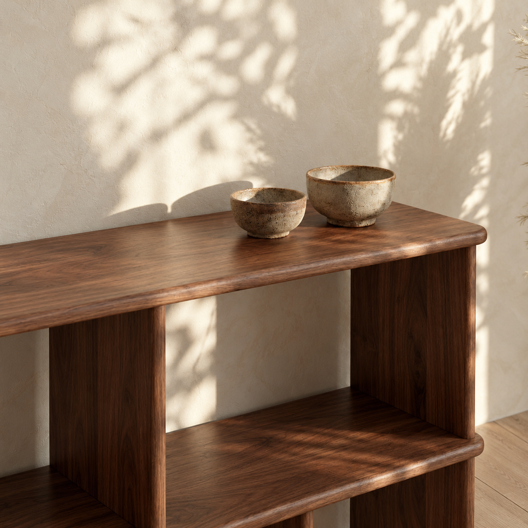 Close-up of the top of the horizontal bookshelf in walnut, with two stone bowls in dappled sunlight.