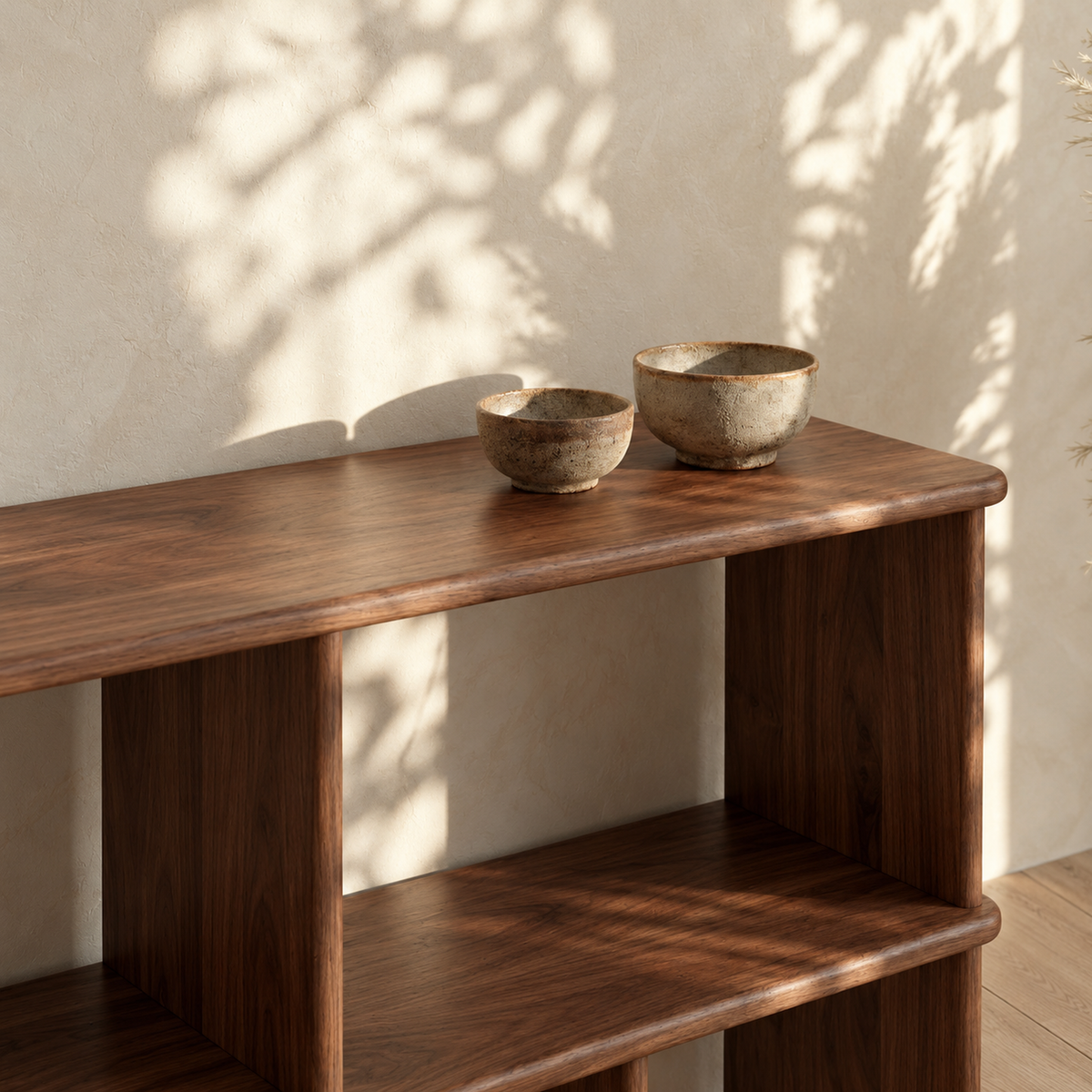 Close-up of the top of the horizontal bookshelf in walnut, with two stone bowls in dappled sunlight.