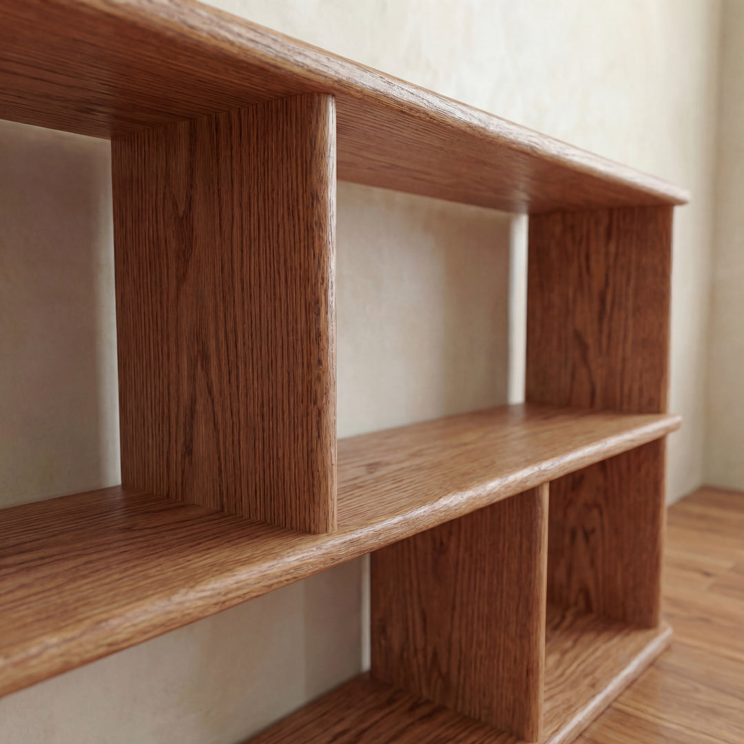 A close-up of the Horizontal bookshelf in red oak, handmade in Vancouver, featuring three levels with vertical dividers, set against a light wall on a wooden floor.