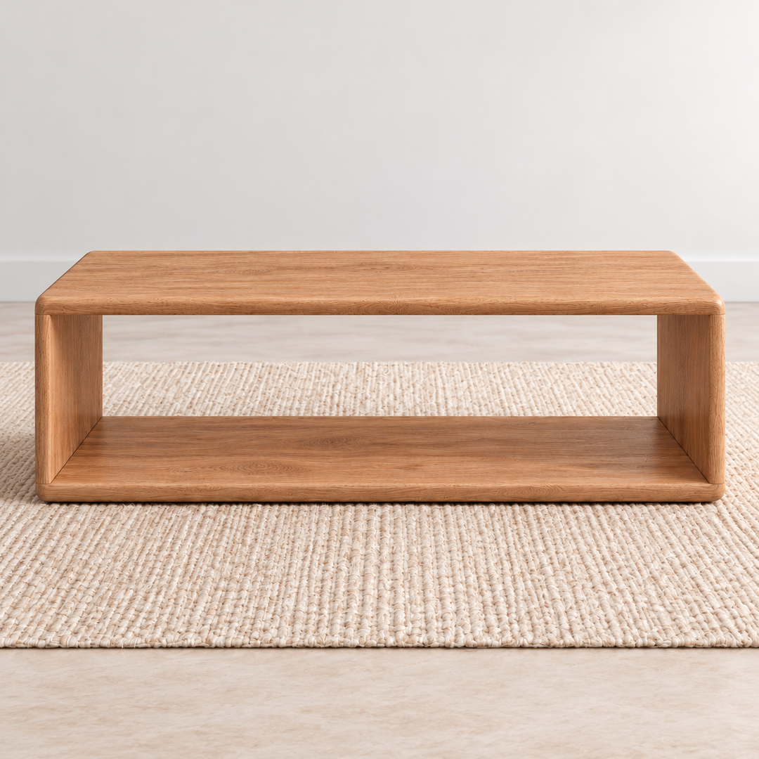 A Japandi coffee table in red oak: a low, open rectangle with softly rounded corners and a lower shelf, on a woven jute rug against a plain light wall.