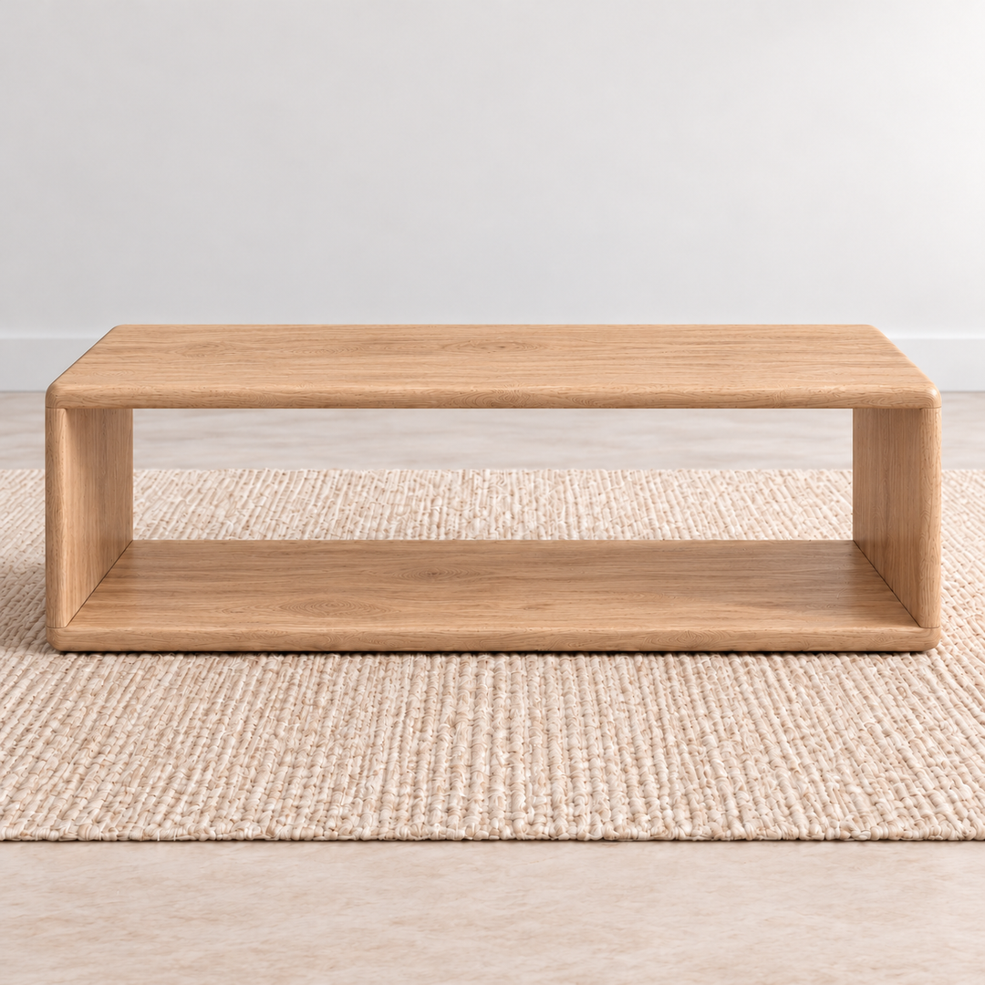 A Japandi coffee table in white oak: a low, open rectangle with softly rounded corners and a lower shelf, on a woven jute rug against a plain light wall.