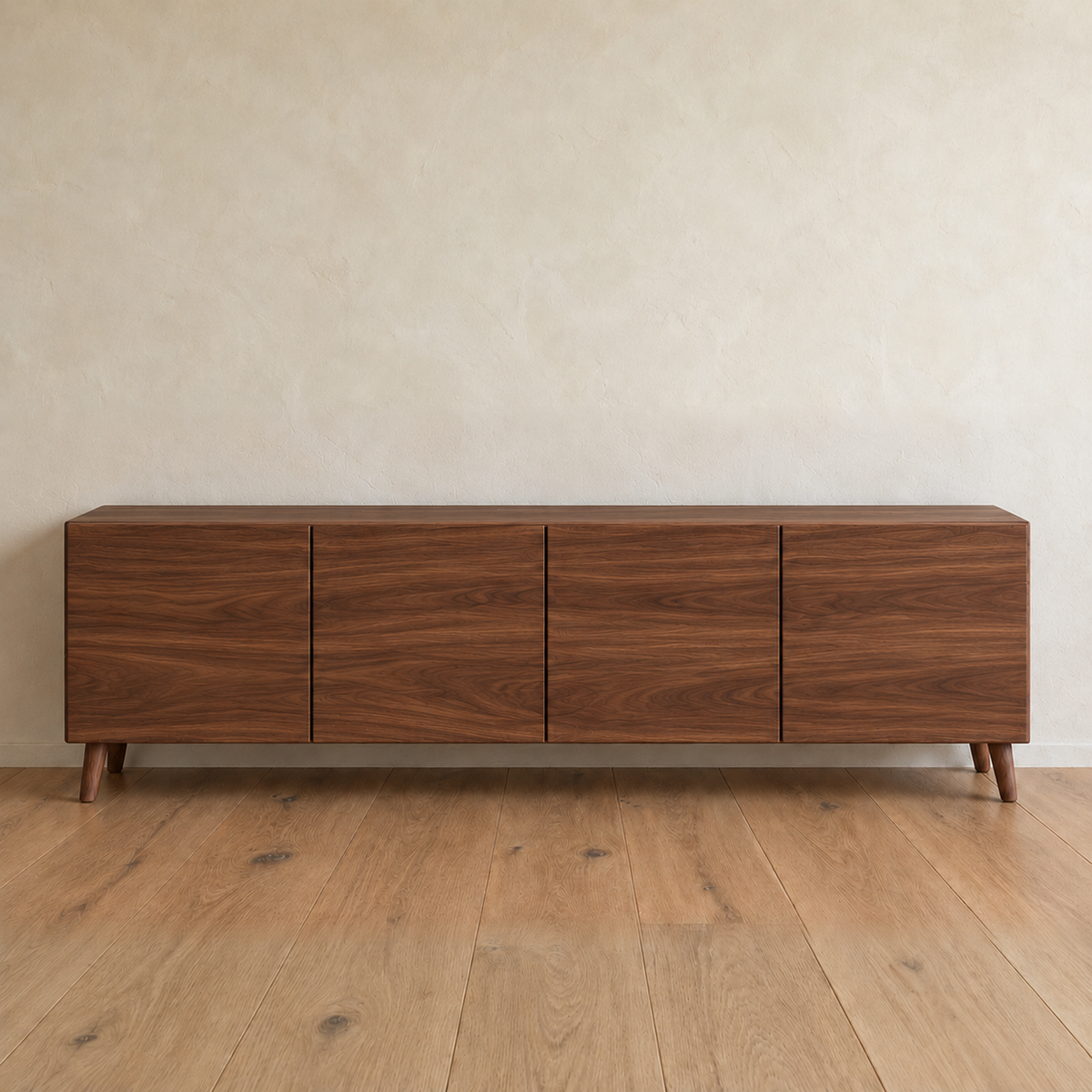 A media console in walnut with four flat doors and tapered legs, against a plain plaster wall on a wood floor.