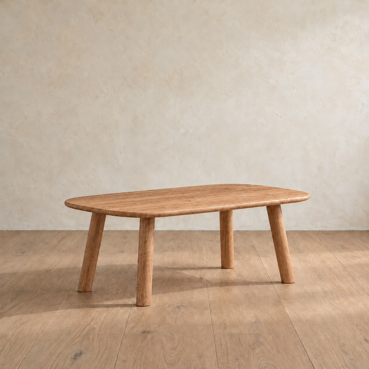 A minimalist coffee table in red oak with a slim top, softly rounded corners and four splayed round legs, against a plain plaster wall.