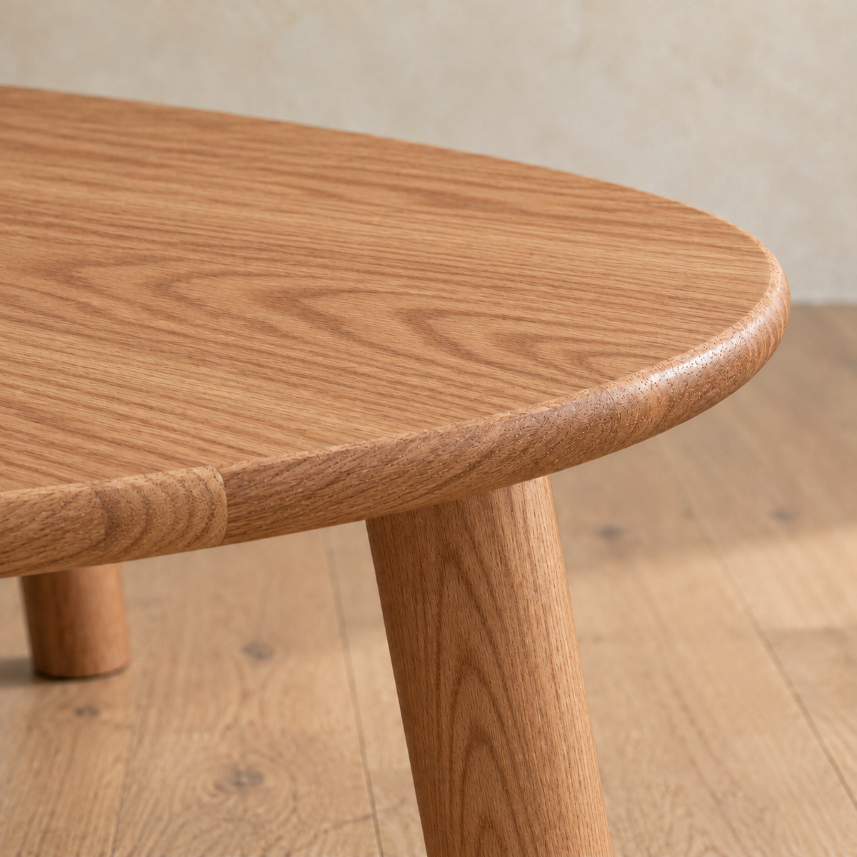 Close-up of the minimalist coffee table in red oak, showing the softly rounded edge of the top and a round leg.