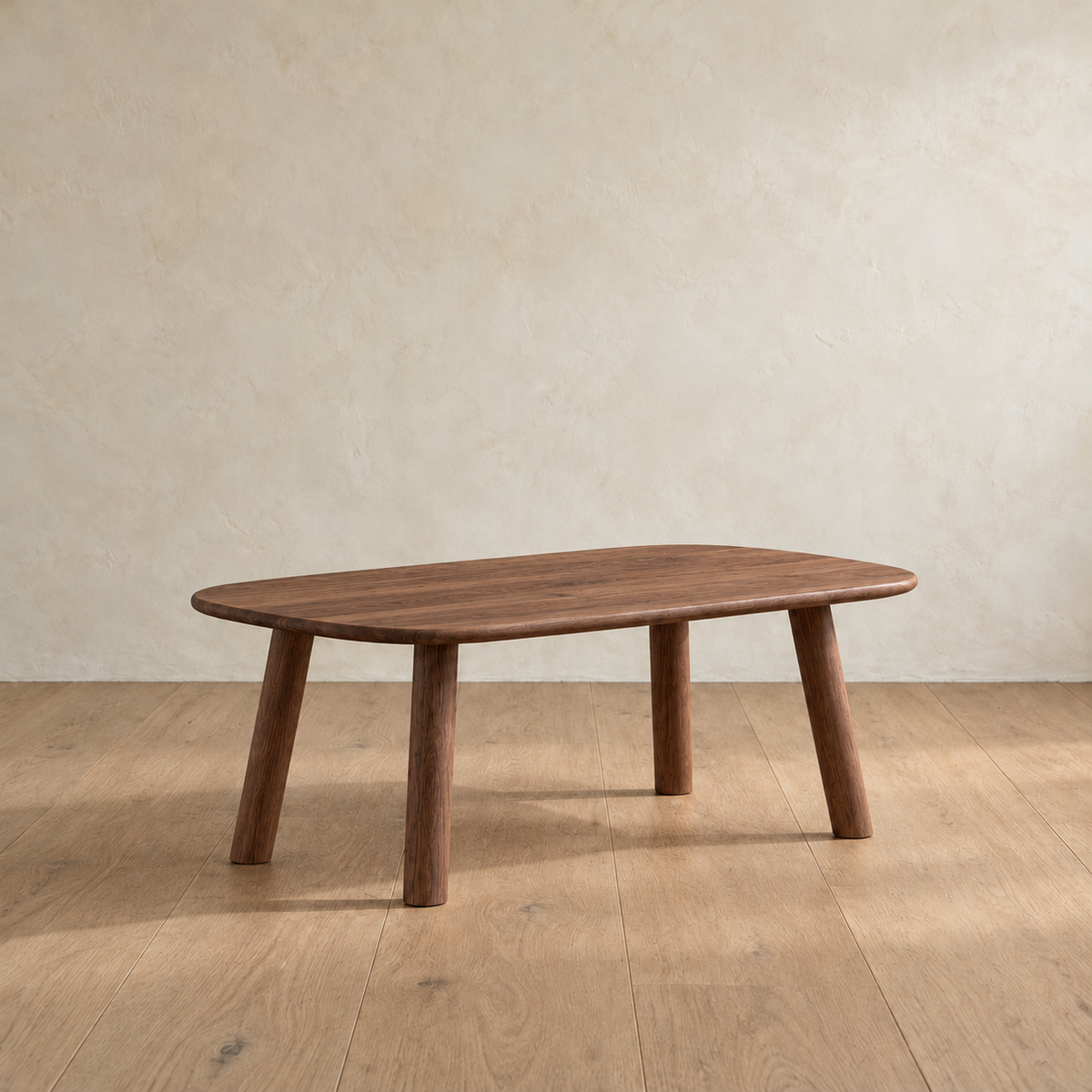 A minimalist coffee table in walnut with a slim top, softly rounded corners and four splayed round legs, against a plain plaster wall.