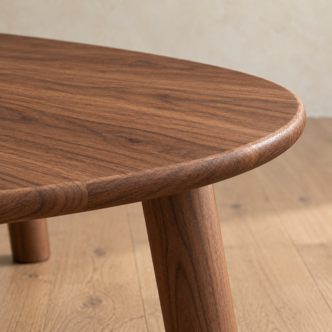Close-up of the minimalist coffee table in walnut, showing the softly rounded edge of the top and a round leg.