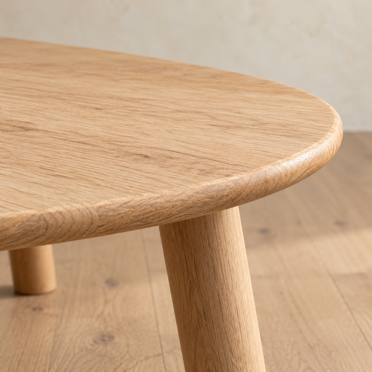 Close-up of the minimalist coffee table in white oak, showing the softly rounded edge of the top and a round leg.