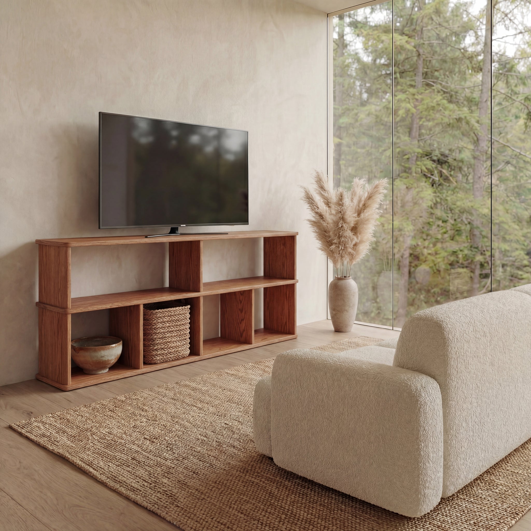 A modern living room features a 65 inch bookshelf TV stand in red oak holding a TV, decorative accents, a large beige sofa, a woven rug, and floor-to-ceiling windows overlooking lush green trees.