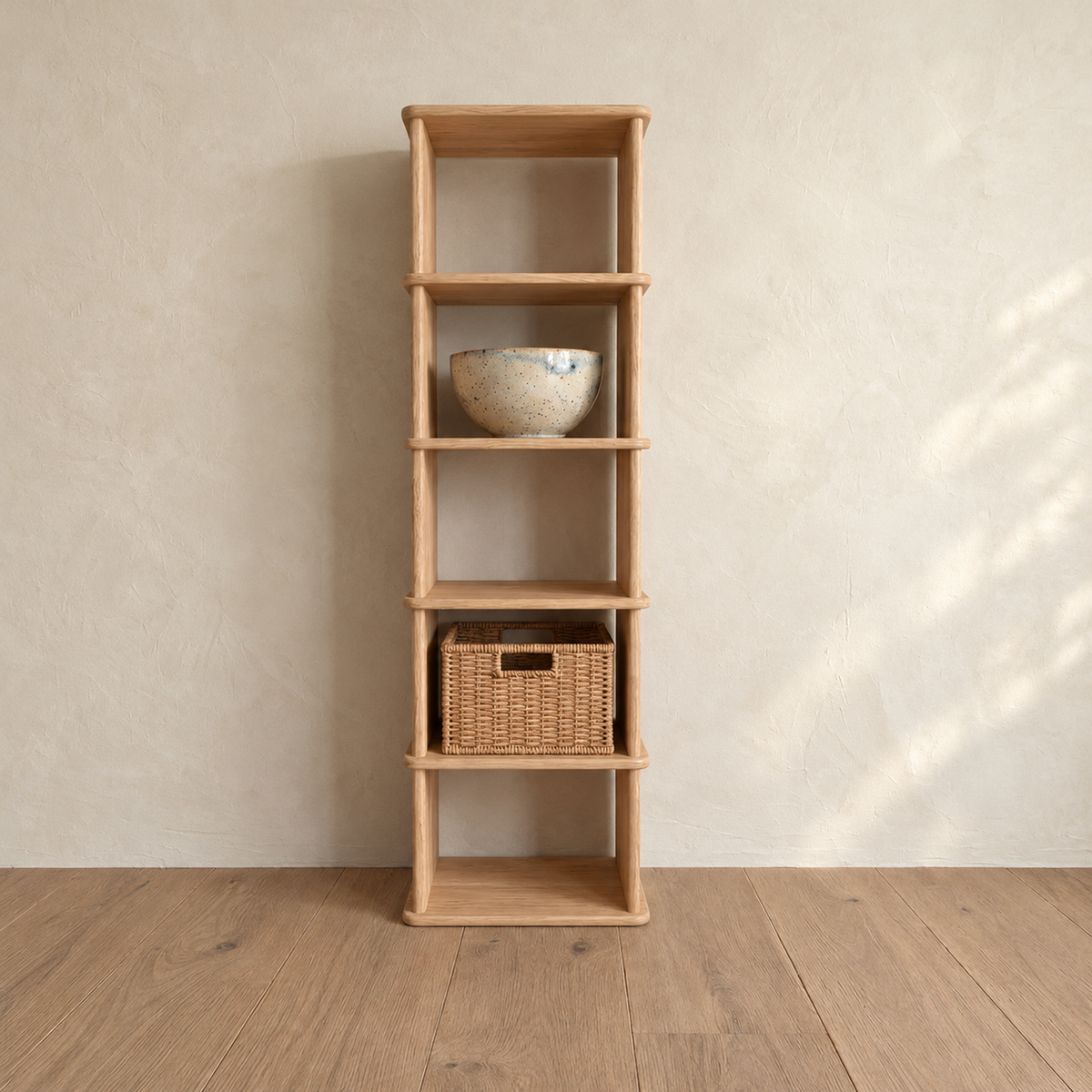 The narrow bookshelf in white oak against a plaster wall, with a ceramic bowl and a woven basket on its shelves.