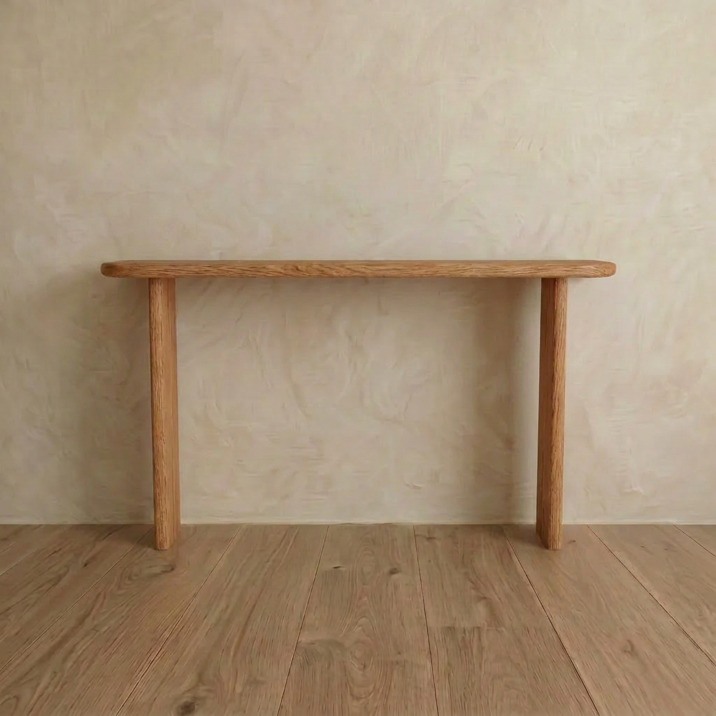The Narrow console table in red oak, handmade in Vancouver from solid red oak, stands against a beige textured wall on a wooden floor, supported by the wall on one side with just two legs for a minimalist look.