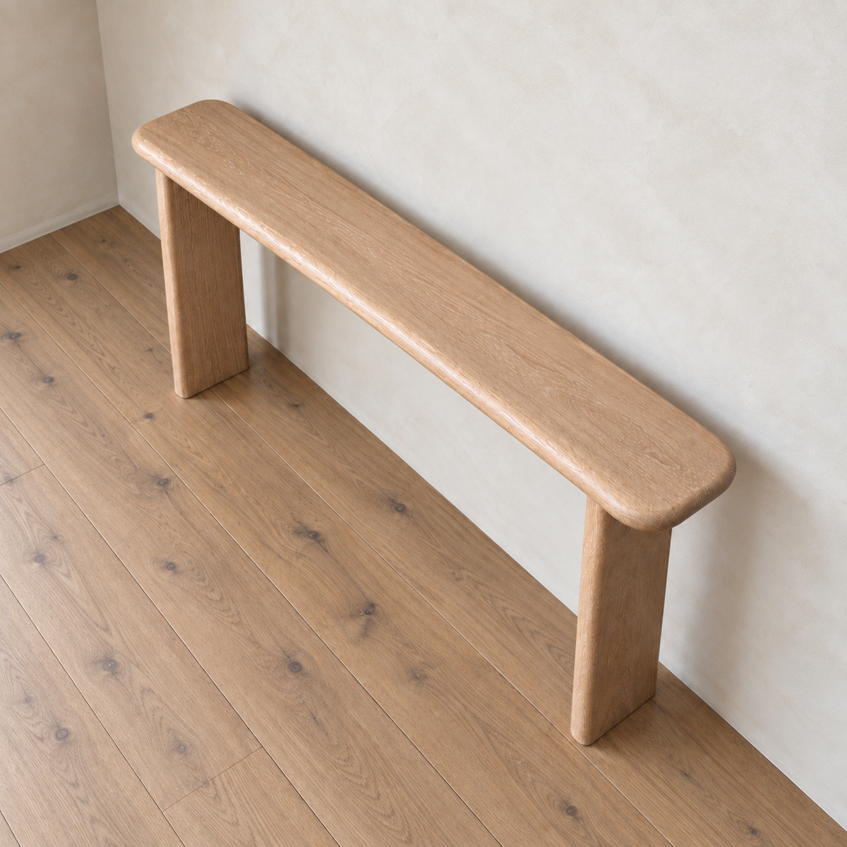 A simple, handmade in Vancouver narrow console table in white oak with rounded edges sits against a beige wall on a light wood floor, viewed from above at an angle.