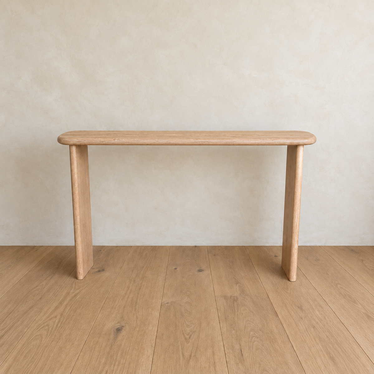 The Narrow console table in white oak is a minimalist, three-legged design with rounded edges, crafted from solid white oak. Handmade in Vancouver, each table stands on a wooden floor against a light beige wall and offers exceptional quality and unique character.