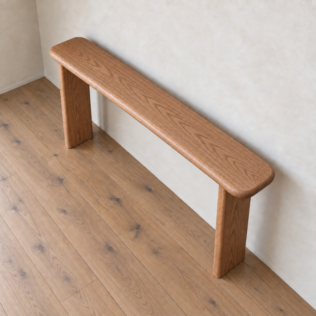 Narrow console table in red oak, handmade in Vancouver with a minimalist design featuring rounded edges and three sturdy legs, shown against a beige wall on a light brown wooden floor. Crafted from solid red oak, its simple modern aesthetic makes it versatile enough to function as either a bench or a console table in various spaces.