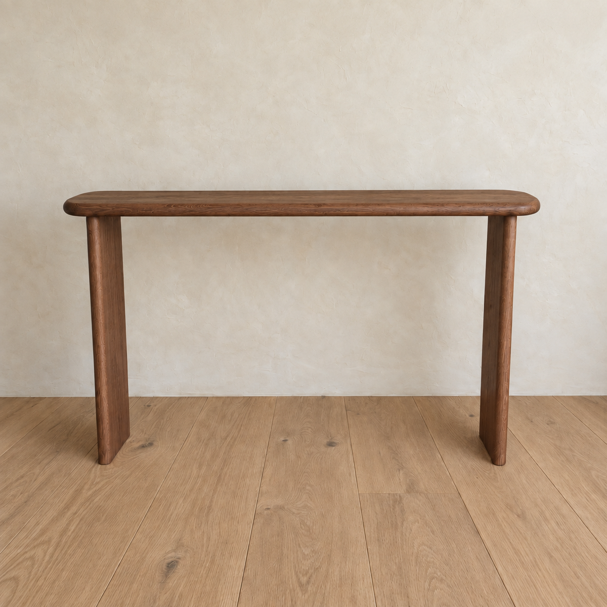 The Narrow console table in walnut, a simple handmade piece with rounded edges and three legs crafted from solid walnut, stands on a light wood floor against a beige textured wall.