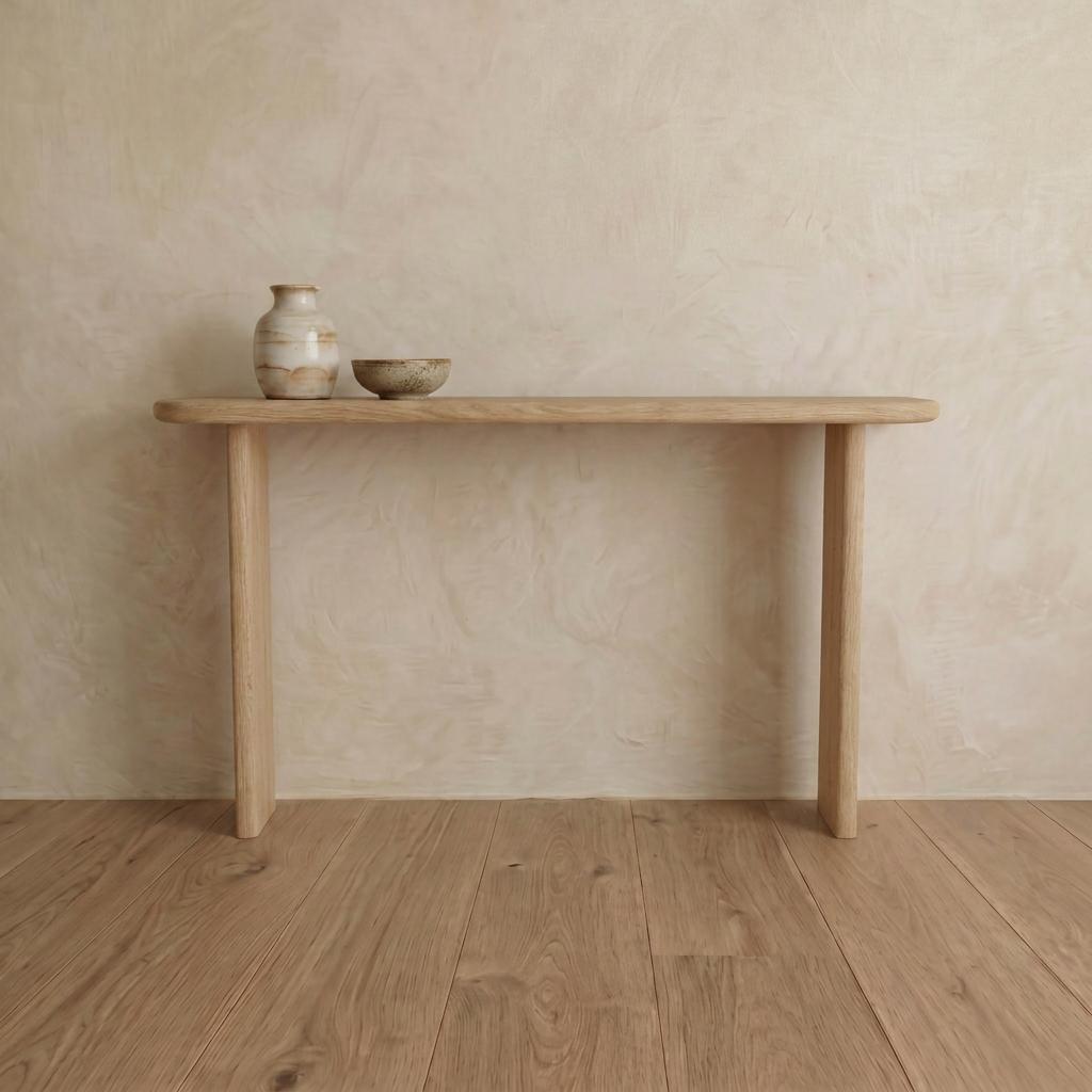 The Narrow console table in white oak, handmade in Vancouver, stands against a beige textured wall on a wooden floor. On the table sit two ceramic pieces: a small vase and a bowl.