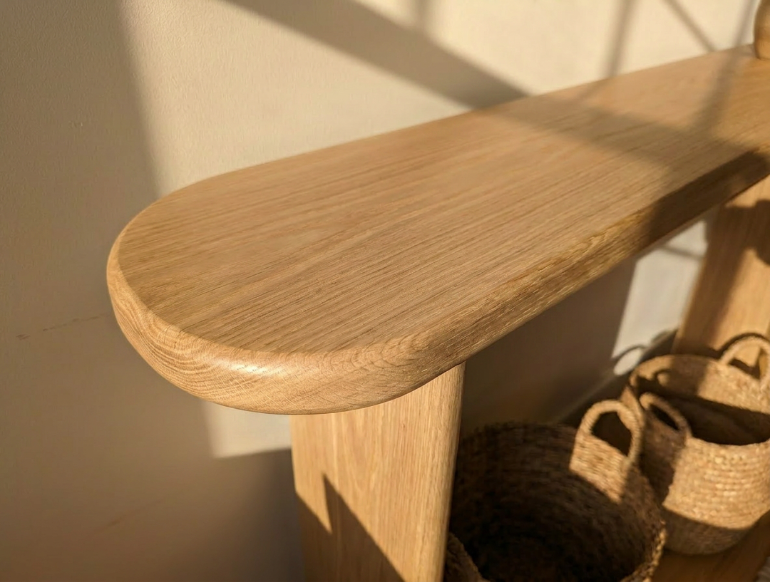 Close-up of the Narrow console table in white oak with rounded edges, sunlight casting gentle shadows. Handmade in Vancouver, it sits above two woven baskets, enhancing the warm and calm atmosphere.
