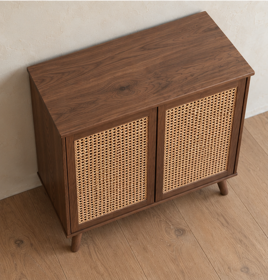 The rattan cabinet in walnut seen from above at an angle, showing the solid walnut top and the woven cane in the doors.