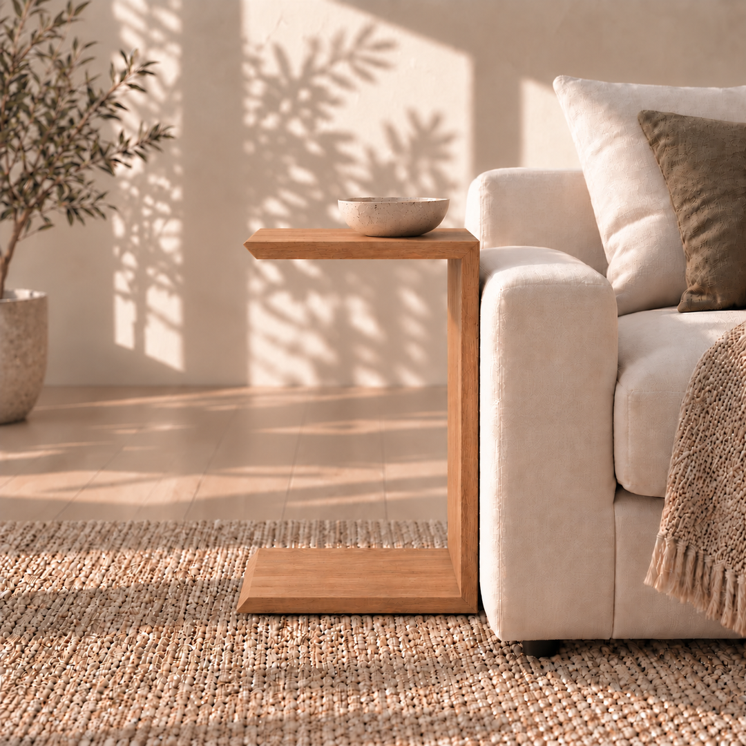 C-shaped red oak Sofa side table in red oak holding a shallow bowl next to a light-colored sofa.