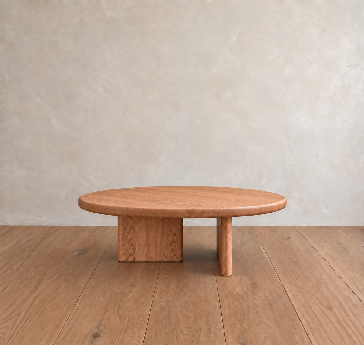 A Round coffee table in red oak with a modern handmade design, featuring a solid red oak top and two distinctive rectangular legs, sits on a wooden floor against a light beige textured wall.