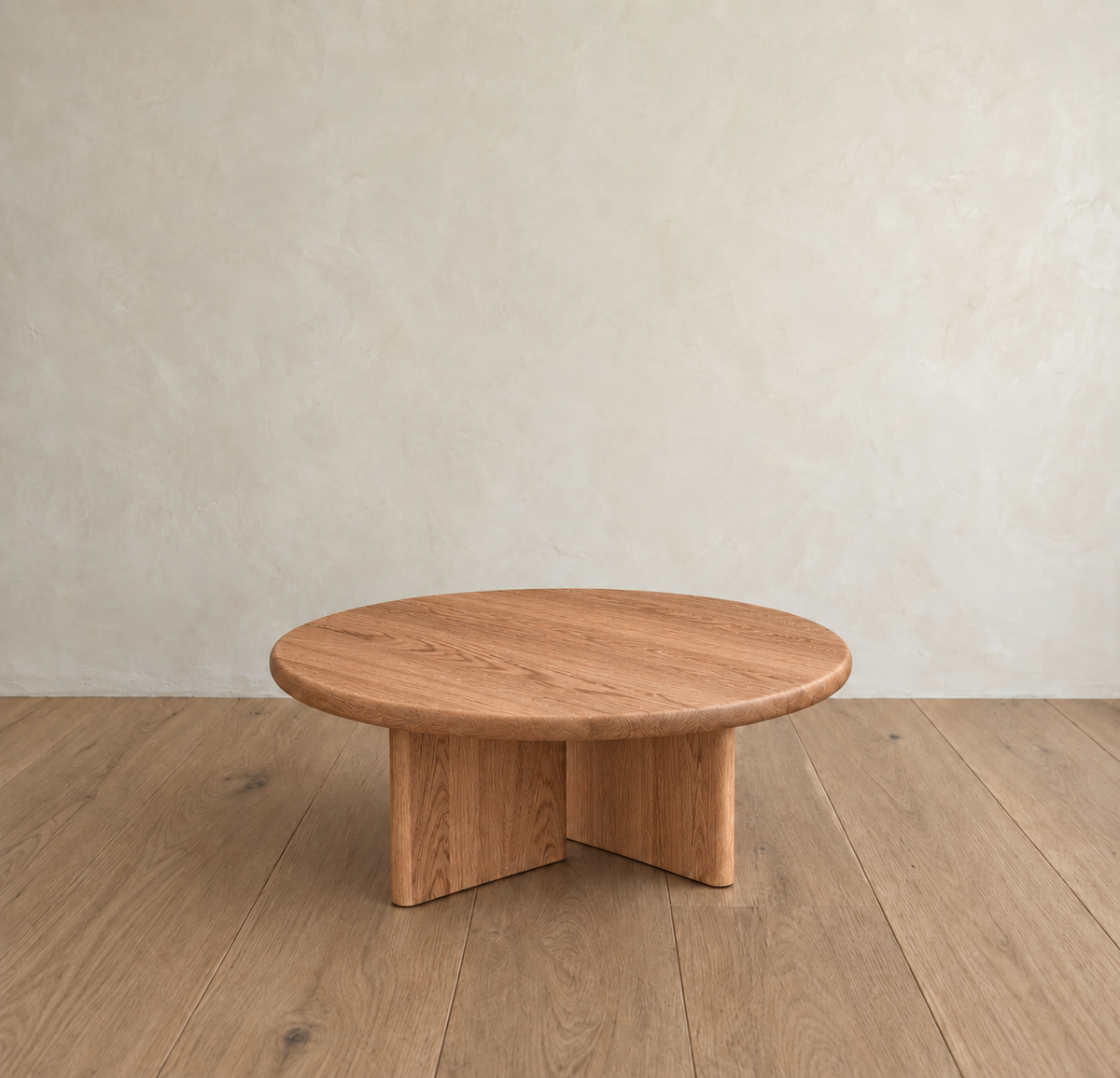 The Round coffee table in red oak, handmade in Vancouver with a minimalist design, sits on a wooden floor against a light beige textured wall.